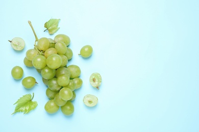 Bunch of ripe grapes with green leaves on light blue background, flat lay. Space for text