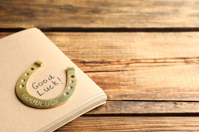 Notebook with phrase GOOD LUCK and horseshoe on wooden table, closeup. Space for text
