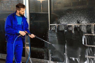 Worker cleaning auto mats with high pressure water jet at car wash