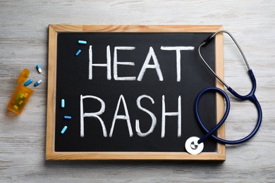 Blackboard with words Heat Rash, stethoscope and pills on wooden table, flat lay