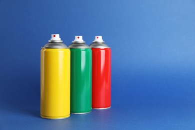 Photo of Colorful cans of spray paints on blue background. Space for text
