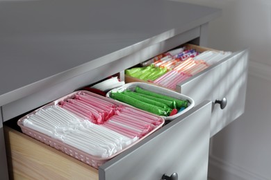 Open cabinet drawers with menstrual pads, tampons and pantyliners indoors, closeup