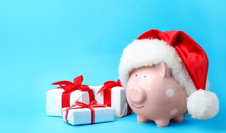 Piggy bank with Santa hat and gift boxes on light blue background