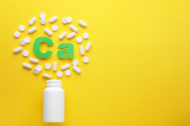 Pills, open bottle and calcium symbol made of green letters on yellow background, flat lay. Space for text