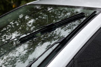 Photo of Wipers cleaning raindrops from car windshield outdoors