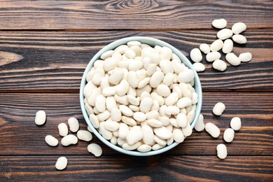 Raw white beans and bowl on wooden table, flat lay