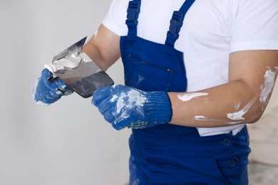 Worker with putty knives and plaster near wall indoors, closeup. Home renovation