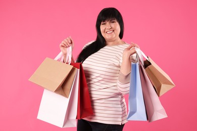 Beautiful overweight mature woman with shopping bags on pink background