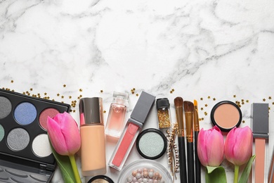 Makeup products and flowers on marble background, flat lay with space for text