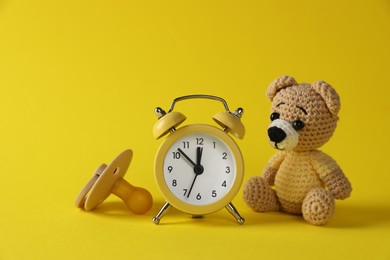 Photo of Alarm clock, toy bear and baby dummy on yellow background. Time to give birth