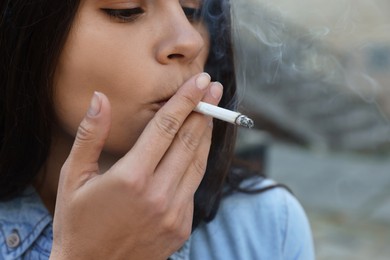 Young woman smoking cigarette outdoors, closeup view