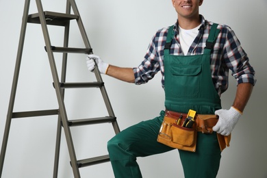 Professional builder near metal ladder on light background, closeup