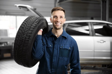 Young mechanic with car tire in service center