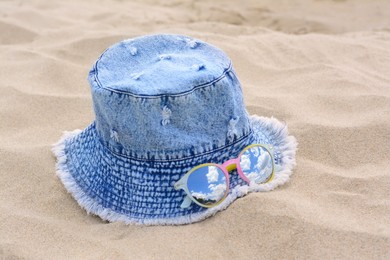 Photo of Jeans hat and sunglasses on sand, closeup. Beach accessories