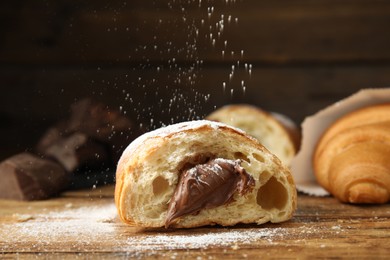 Sprinkling sugar powder onto tasty croissant with chocolate on wooden table