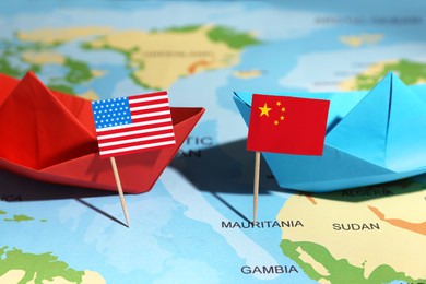 Paper boats with USA and China flags on world map, closeup. Trade war concept