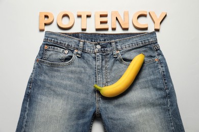Men jeans with banana and word Potency made of wooden letters on light grey background, flat lay