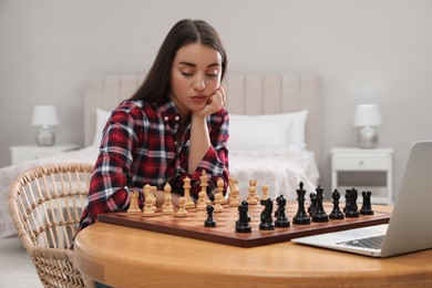 Thoughtful young woman playing chess with partner through online video chat at home