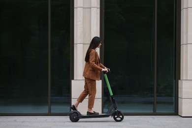 Businesswoman riding electric kick scooter on city street