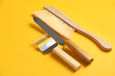 Three different beekeeping tools on yellow background