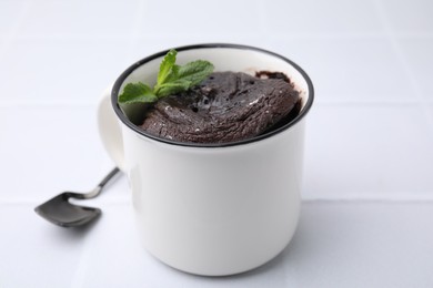 Photo of Tasty chocolate mug pie and spoon on white table. Microwave cake recipe
