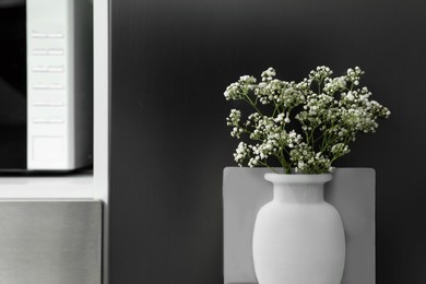 Silicone vase with beautiful gypsophila flowers on fridge in kitchen, space for text