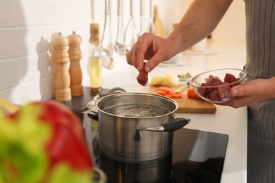 Man putting meat into pot to make bouillon in kitchen, closeup. Homemade recipe