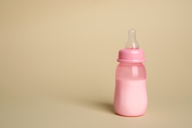 Photo of Feeding bottle with infant formula on beige background. Space for text