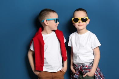 Portrait of cute twin brothers with sunglasses on color background