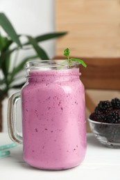 Delicious blackberry smoothie in mason jar and berries on white table indoors