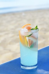 Photo of Glass of refreshing drink with grapefruit and mint on blue lounger at beach