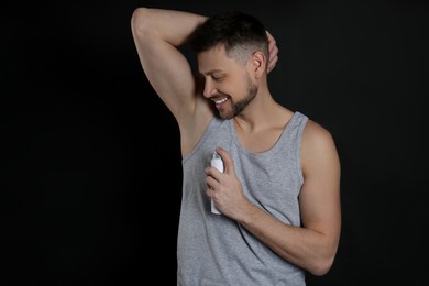 Handsome man applying deodorant on black background