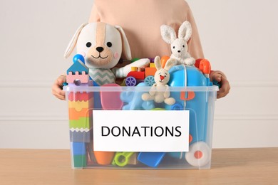 Little girl holding donation box with toys against light background, closeup