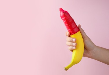 Woman holding banana in condom on pink background, closeup and space for text. Safe sex concept