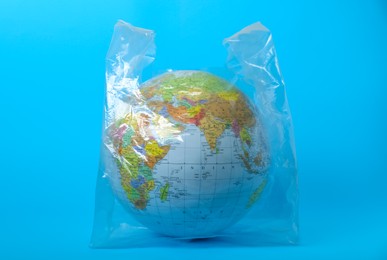 Globe in plastic bag on turquoise background. Environmental conservation