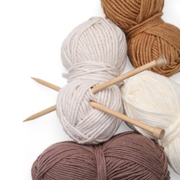 Soft woolen yarns and knitting needles on white background, top view
