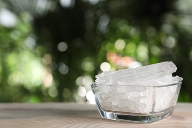Menthol crystals in glass bowl on wooden table against blurred background. Space for text