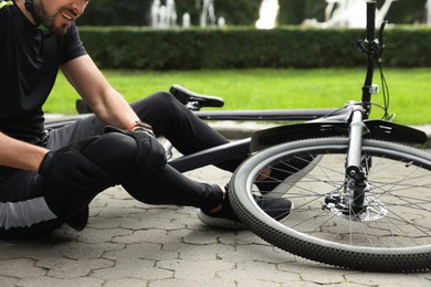 Photo of Man with injured knee near bicycle outdoors, closeup