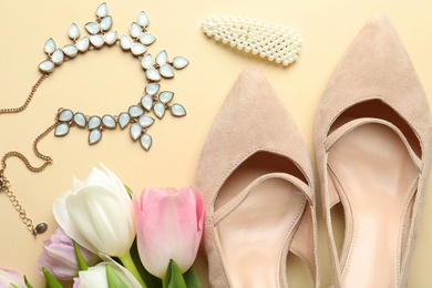 Stylish shoes, beautiful flowers and accessories on beige background, flat lay