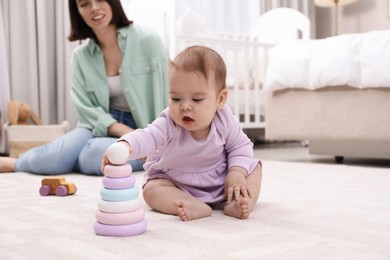 Cute baby girl playing with toy pyramid near mother on floor at home