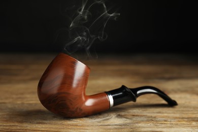 Classic stylish smoking pipe on wooden table, closeup