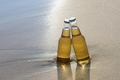 Bottles of cold beer on sandy beach, space for text