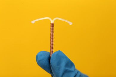 Doctor holding T-shaped intrauterine birth control device on yellow background, closeup