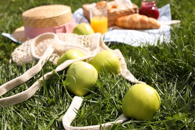 Fresh apples near blanket with juice and croissant on green grass. Picnic season