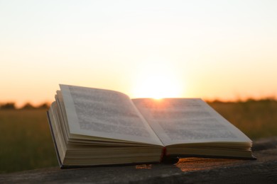 Open book on wooden bench in field at sunset