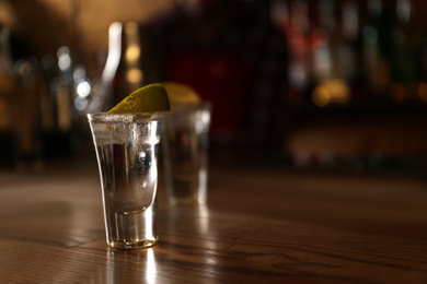 Tequila shot with lime on wooden counter in bar, space for text. Alcoholic cocktail