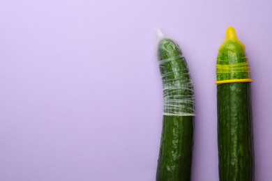 Cucumbers with condoms on lilac background, flat lay and space for text. Safe sex