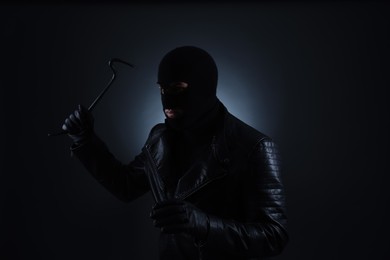 Photo of Man wearing knitted balaclava with crowbar on black background