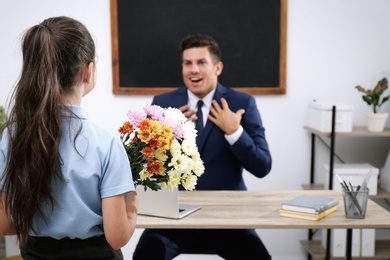 Schoolgirl with bouquet congratulating her  emotional pedagogue in classroom. Teacher's day