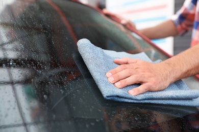 Man cleaning windshield with duster, closeup. Car wash service